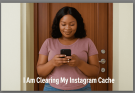 Nigerian woman standing in front of her door using smartphone to clear Instagram cache.